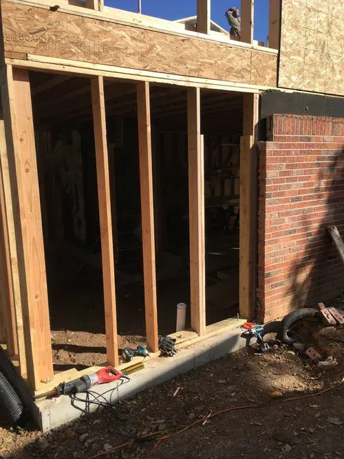 Partially framed doorway opening into a brick building with construction tools and debris on the ground