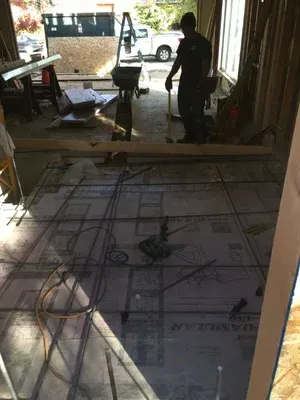 Construction site interior with rebar floor grid, tools, and two people silhouetted near an open doorway