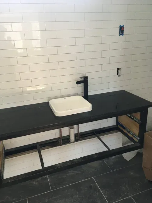 Black countertop with a white sink basin in a tiled bathroom or utility room.