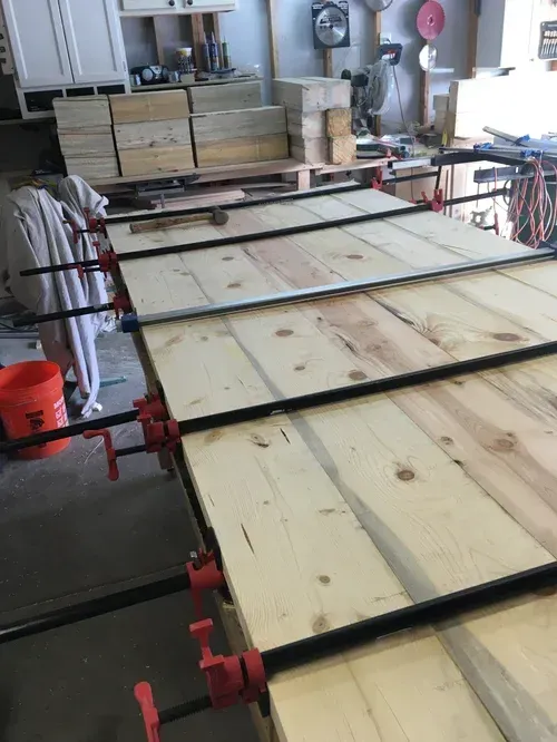Wood boards clamped together in a workshop, forming a large tabletop under construction