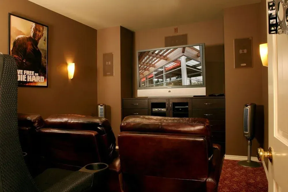 Cozy home theater with leather chairs facing a TV showing a sports arena