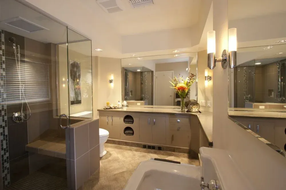 Elegant bathroom with double vanity, large mirrors, glass shower, and warm wall sconces