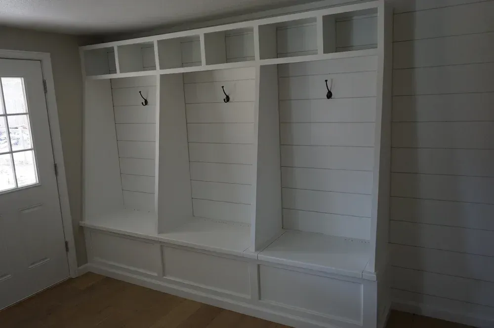 Built-in white mudroom cubbies with hooks, shelves, and bench seating beside a door