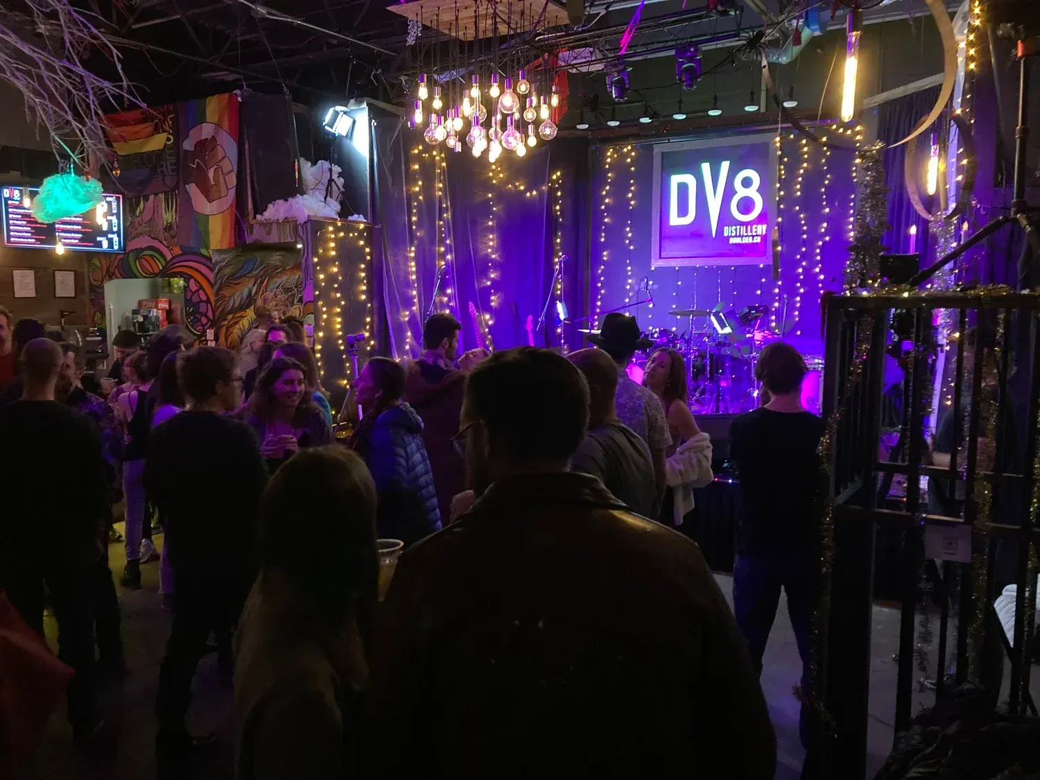 Crowded nightclub with purple lighting and a neon DV8 sign on stage