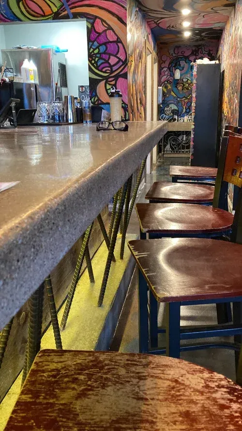 Colorful bar interior with a long counter, stools, and abstract mural walls