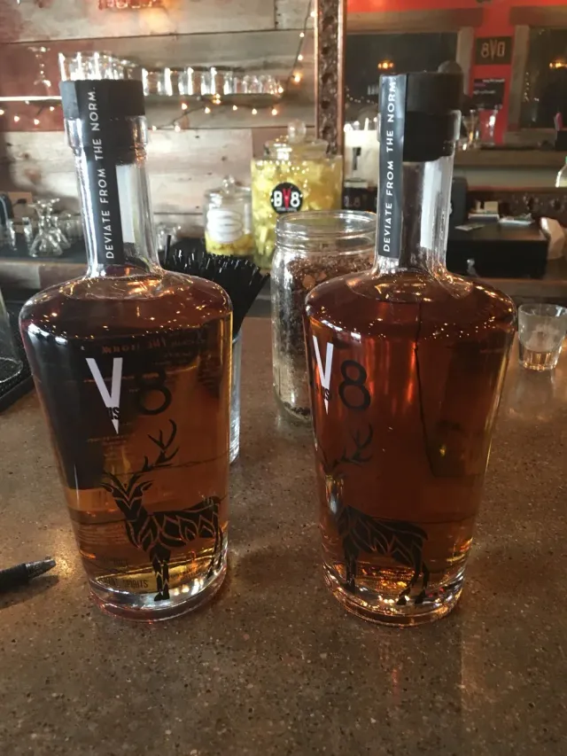 Two bottles of amber liquor on a bar counter, with blurred bottles and glasses in the background.