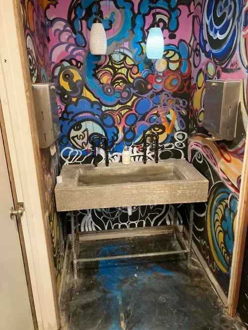 Graffiti-covered bathroom with a stone sink, two pendant lights, and a blue floor