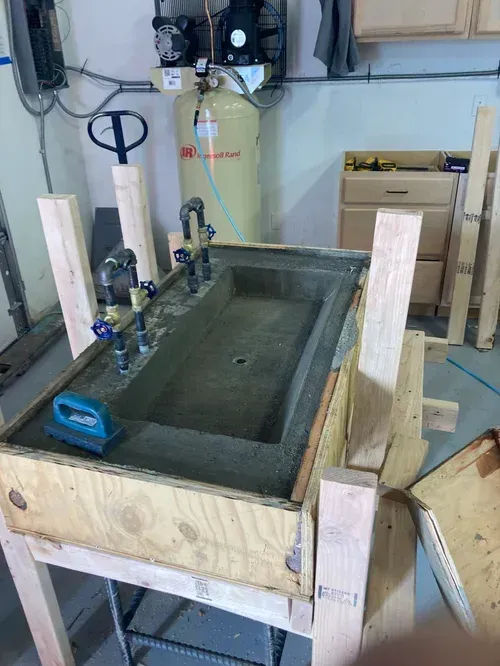 Wooden test setup with a concrete trough, clamps, and a hand pump in a workshop garage