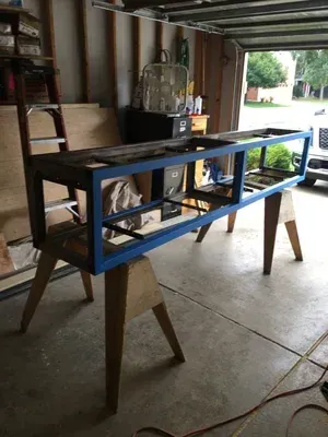 Blue rectangular metal frame on wooden sawhorses in a garage or workshop