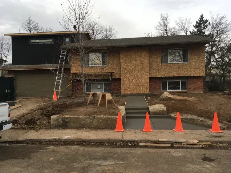 House under renovation with ladder, scaffolding, and orange traffic cones along the curb