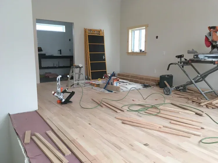Partially renovated room with unfinished wood flooring, tools, wires, and construction materials scattered around