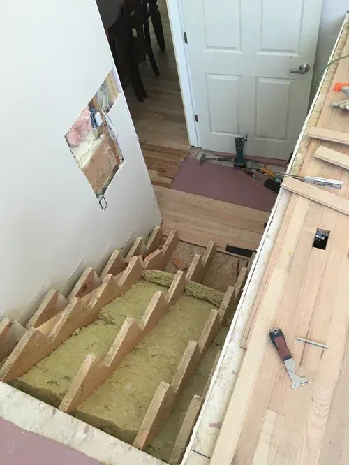 Interior stairwell under construction with exposed wooden steps, white door, and tools on the floor