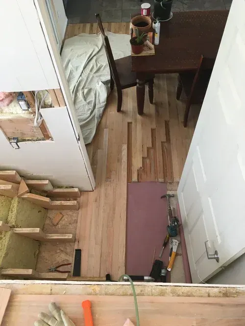 Small room with a bed, wooden chair, side table, and scattered items on the floor.