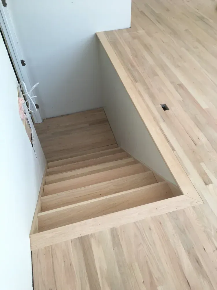 Wooden staircase descending beside a light wood countertop in a modern interior.
