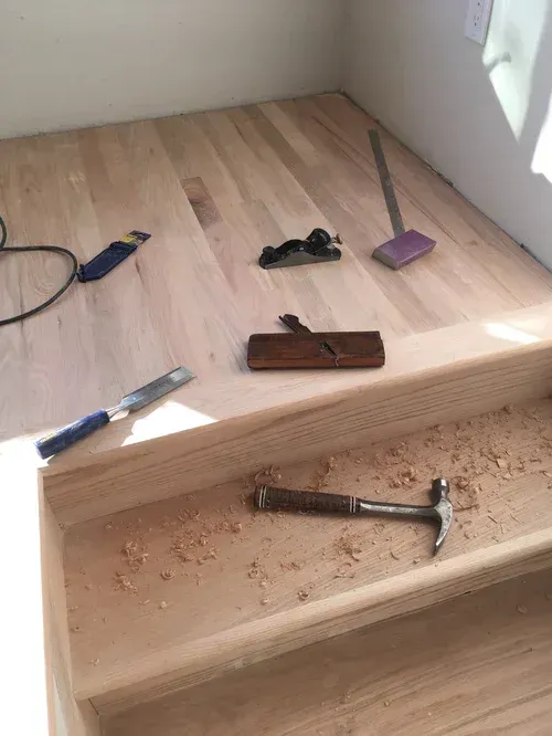 Wooden steps under construction with tools and sawdust scattered on a light wood floor.