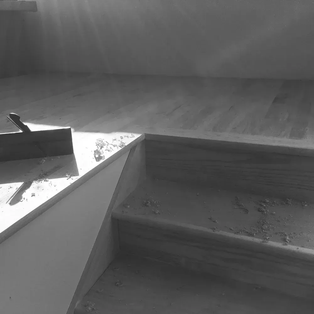 Grayscale view of a stairwell with debris on the steps and a sunlit floor above.