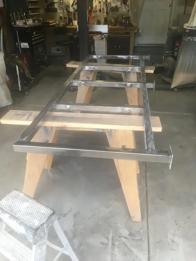 Metal frame on wooden sawhorses in a garage workshop, with a small step stool in the foreground