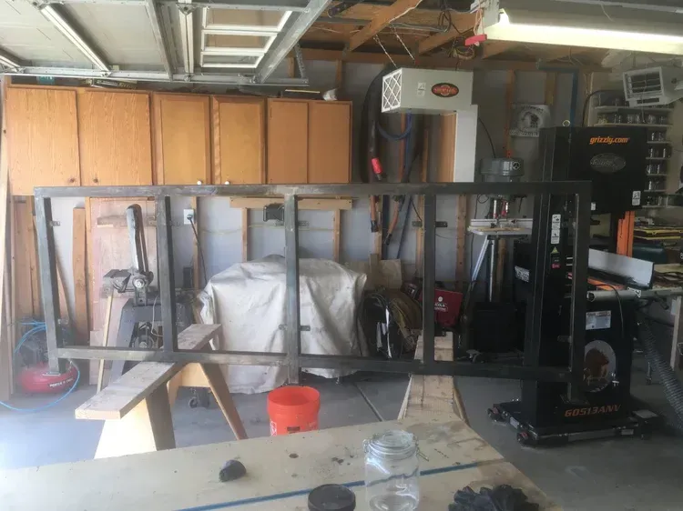 Garage with a large black metal frame, covered items, storage cabinets, and a red bucket on the floor.