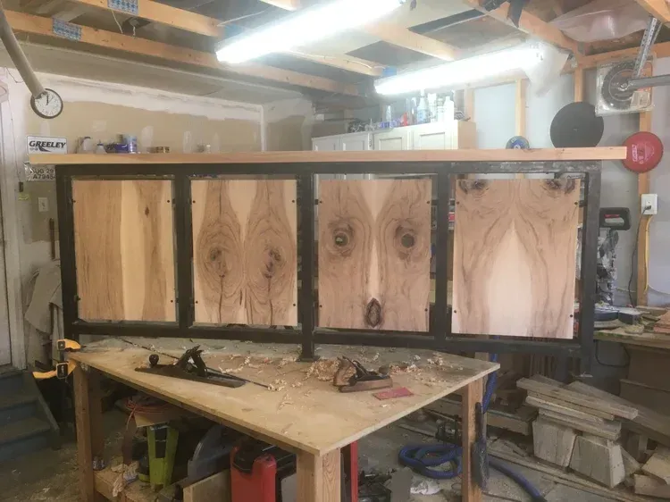 Wood-framed panel with four plywood inserts in a cluttered workshop, resting on a workbench.