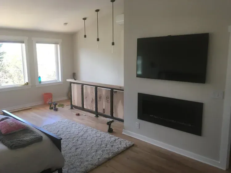 Bright living room with wall-mounted TV, fireplace, windows, rug, and a sofa edge in the foreground