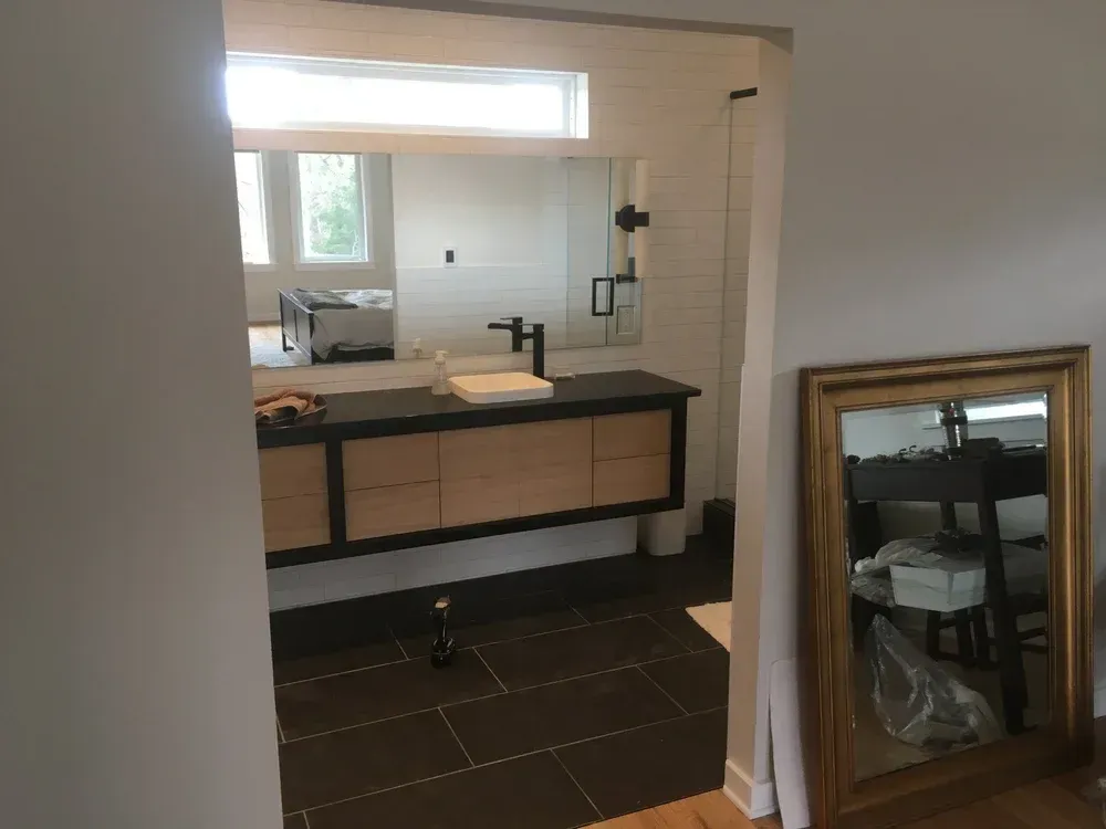 Modern bathroom with a double sink vanity, mirror, window, and framed mirror leaning against the wall