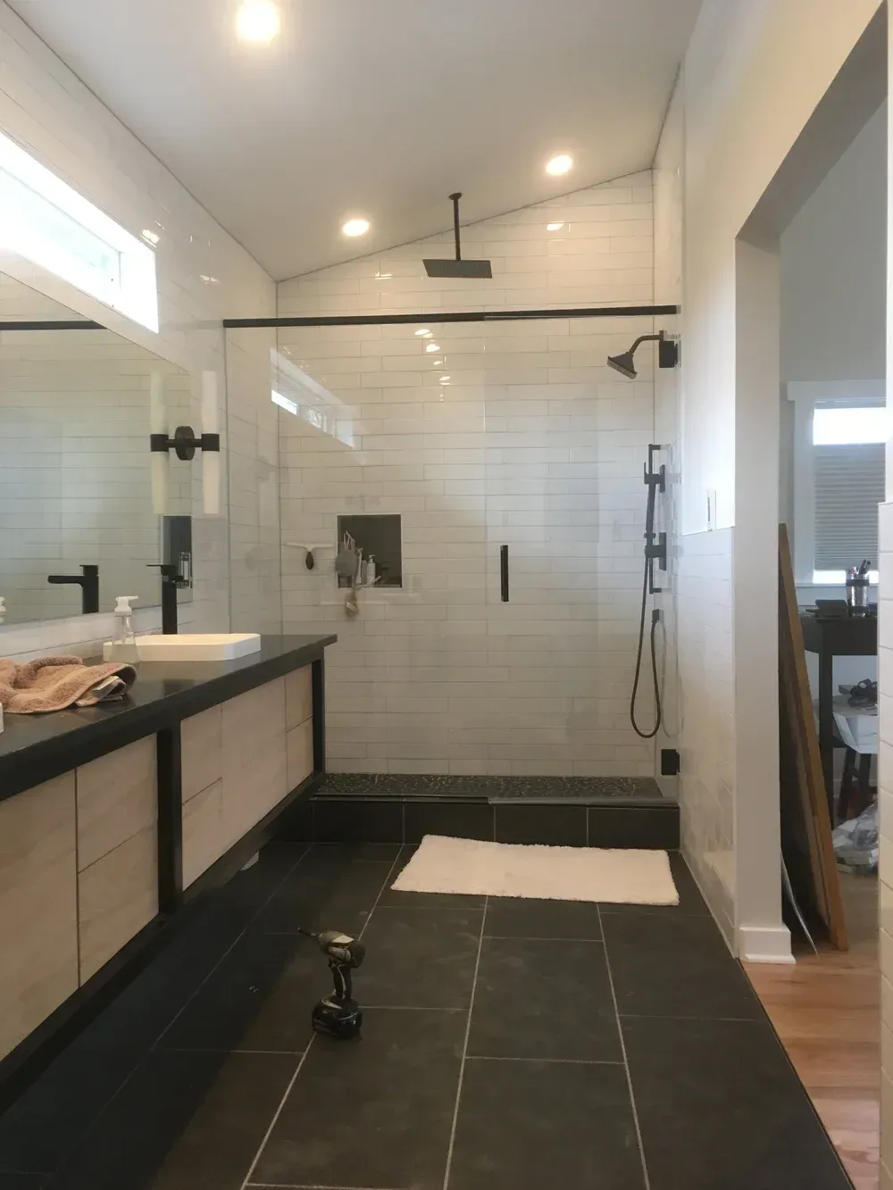 Modern bathroom with a walk-in shower, dark tile floor, vanity, and glass wall near a bedroom doorway