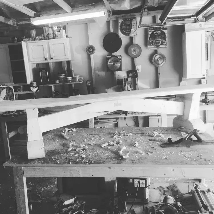 Messy garage workshop with shelves, hanging pots, and a cluttered workbench covered in debris