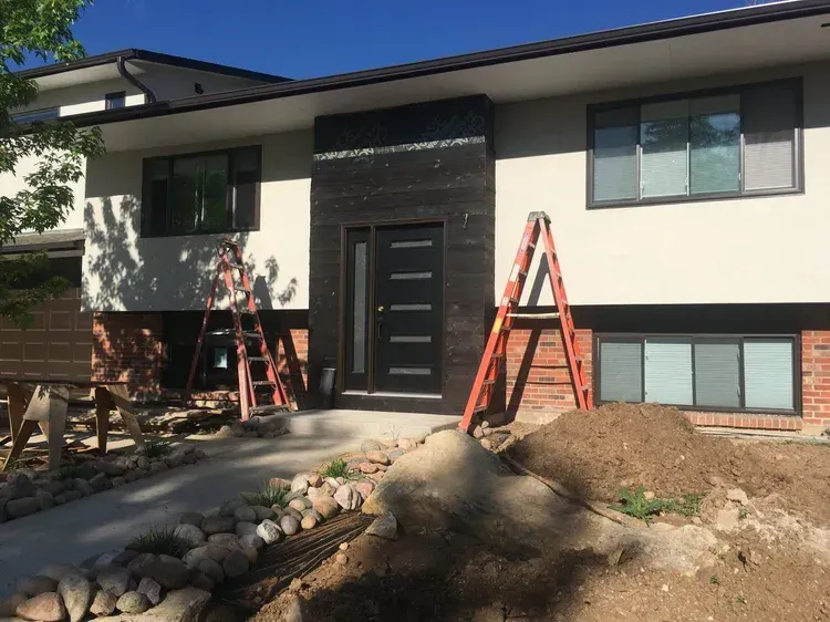 Front of a house with ladders, fresh landscaping, and a dark front door under a blue sky