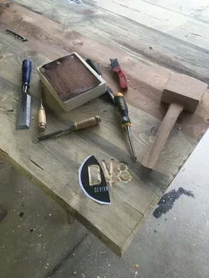 Wooden workbench with chisels, a hammer, pliers, a wooden block, and a small framed tray.