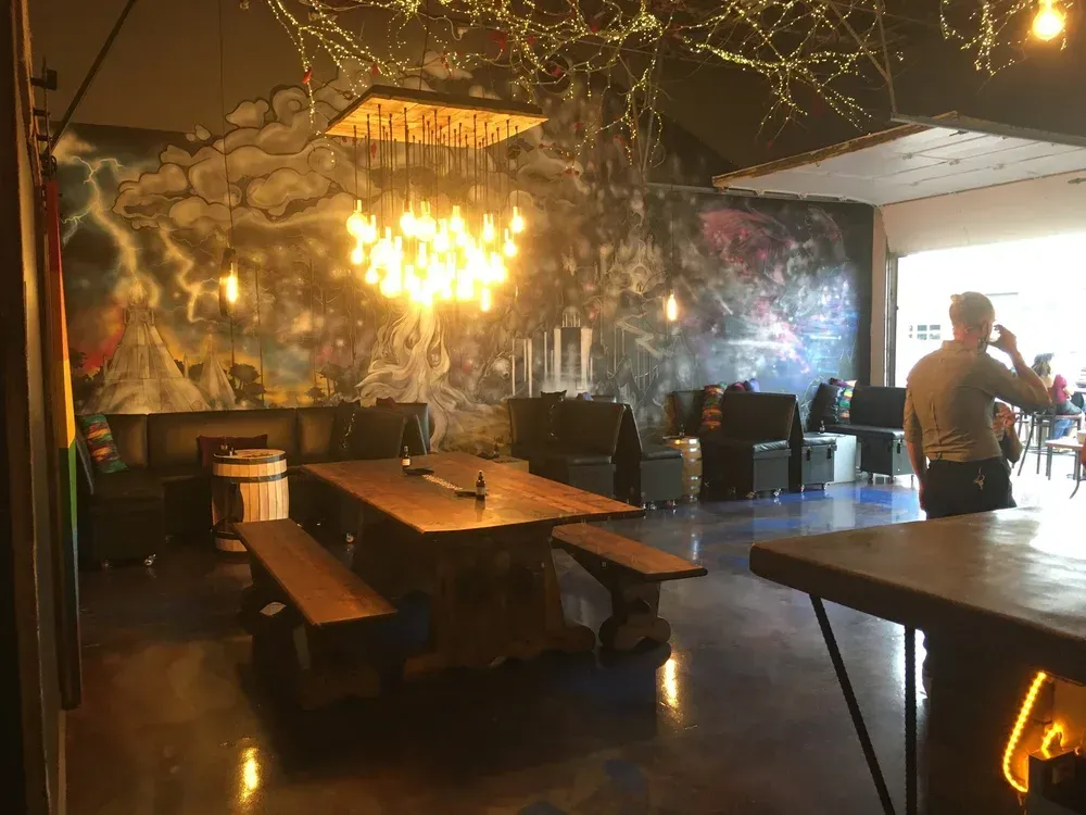 Dim restaurant interior with wooden booths, a chandelier, mural walls, and a person standing near the bar.