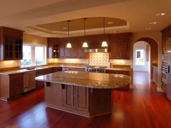 Spacious modern kitchen with dark wood cabinets, granite island, pendant lights, and red hardwood floors