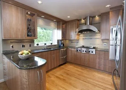 Modern kitchen with wood cabinets, stainless steel appliances, black countertops, and a window over the sink.