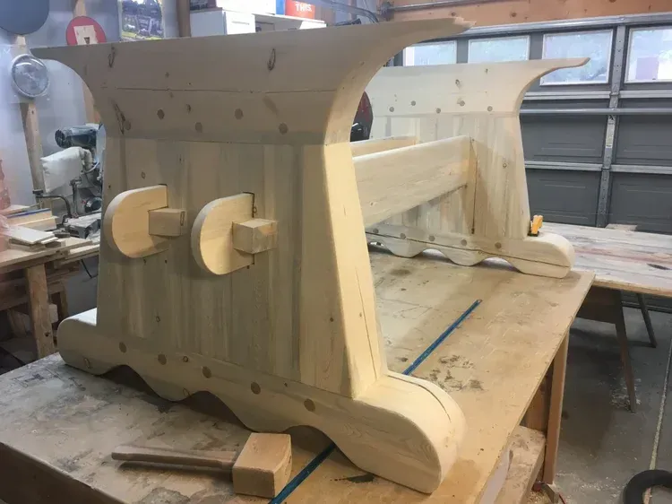 Partially assembled wooden furniture frame in a workshop, with clamps and tools nearby