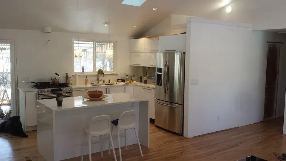 Bright modern kitchen with white island, stainless steel fridge, and wooden floors