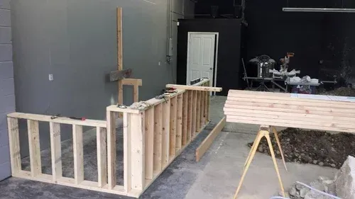 Partially built wooden frame in a workshop or garage, with lumber on sawhorses nearby