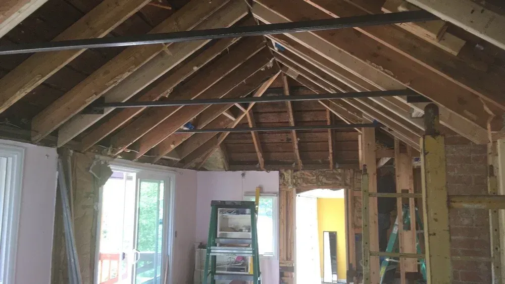 Exposed attic ceiling with wooden rafters and insulation, showing a room under renovation.