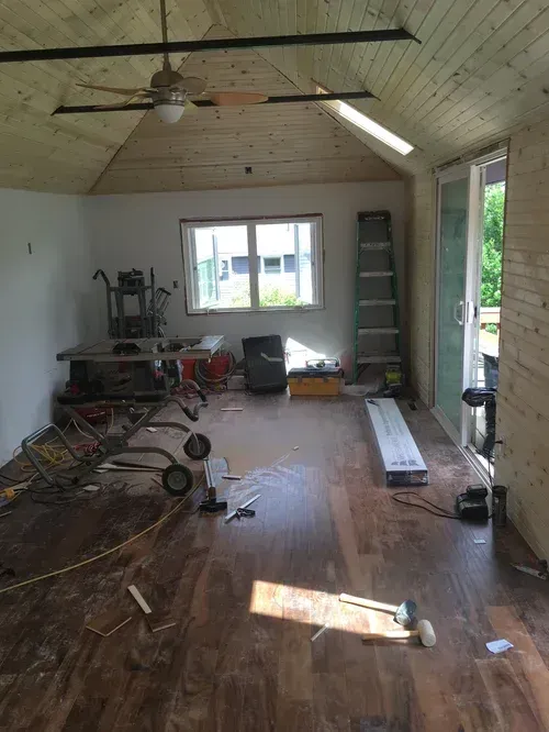 Cluttered garage with tools, ladder, ceiling fan, and sunlight on a wooden floor