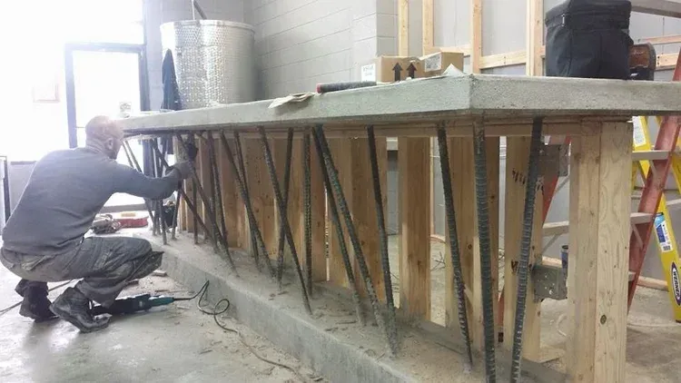 Workers building a large wooden form or mold in an industrial workshop, with a ladder nearby.
