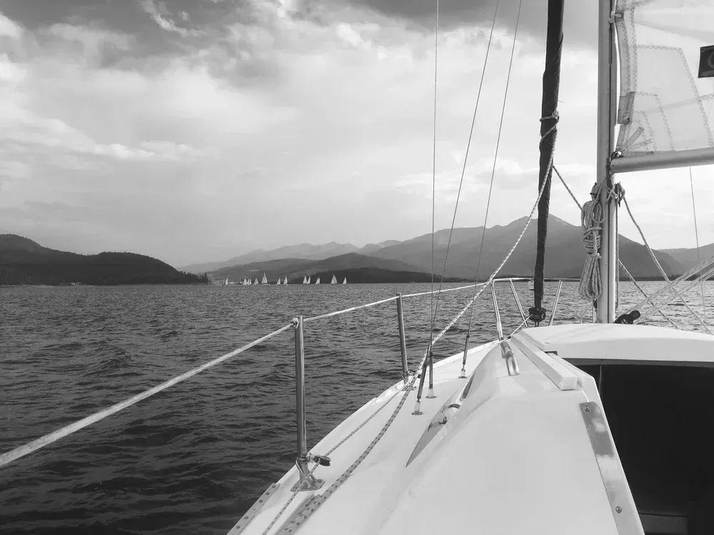 Sailboat deck on calm water with distant mountains under cloudy sky