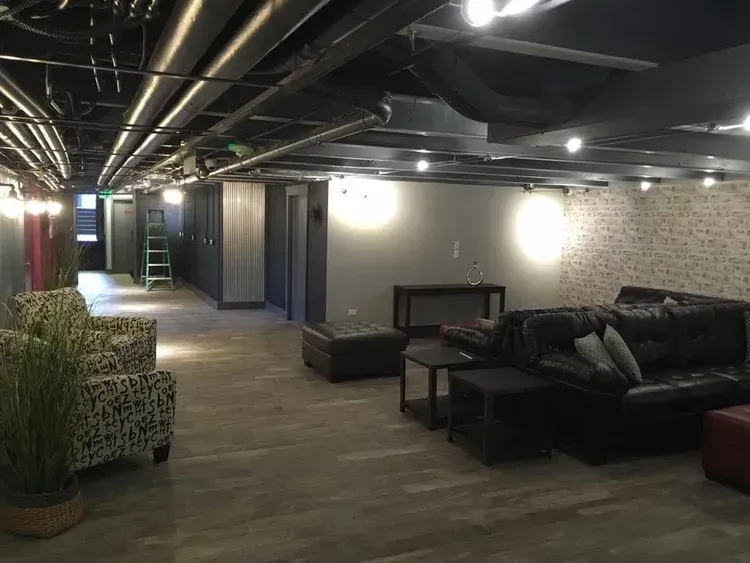 Dim lounge with black leather sofas, low tables, and exposed ceiling lights in a modern hallway