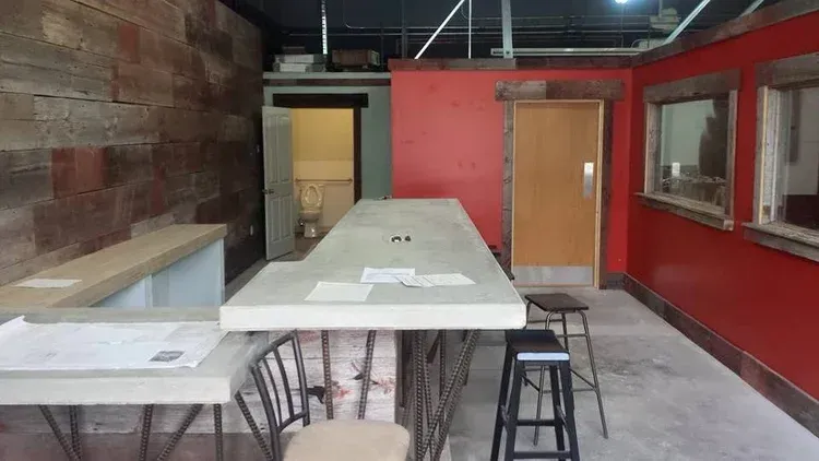 Empty industrial-style room with a long white table, stools, and red walls under construction
