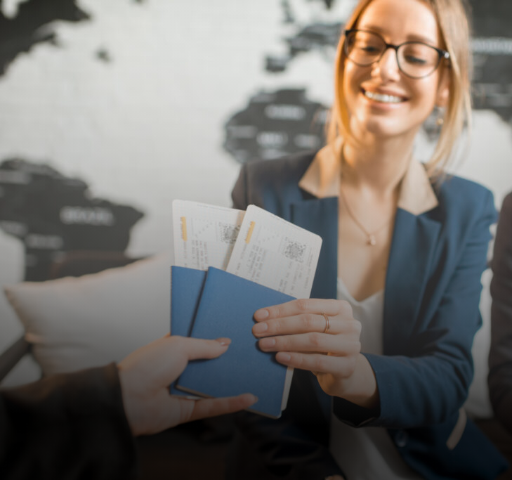 Woman smiles, hands blue passport and tickets to another person. World map background.