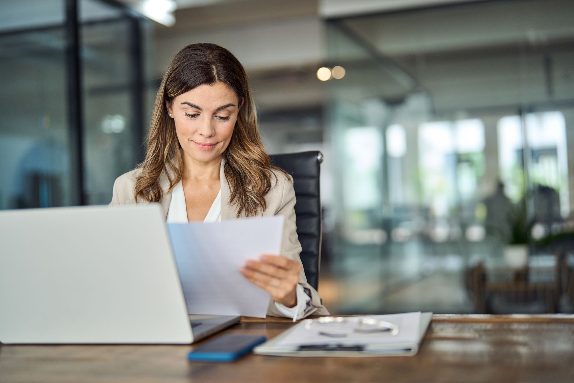 A woman is sitting at a desk with a laptop and a piece of paper.