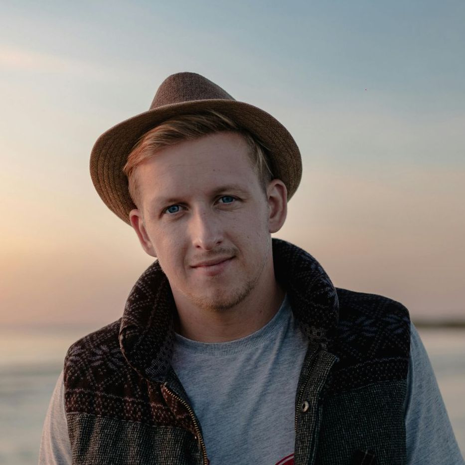 Un homme portant un chapeau et un gilet se tient debout sur la plage.