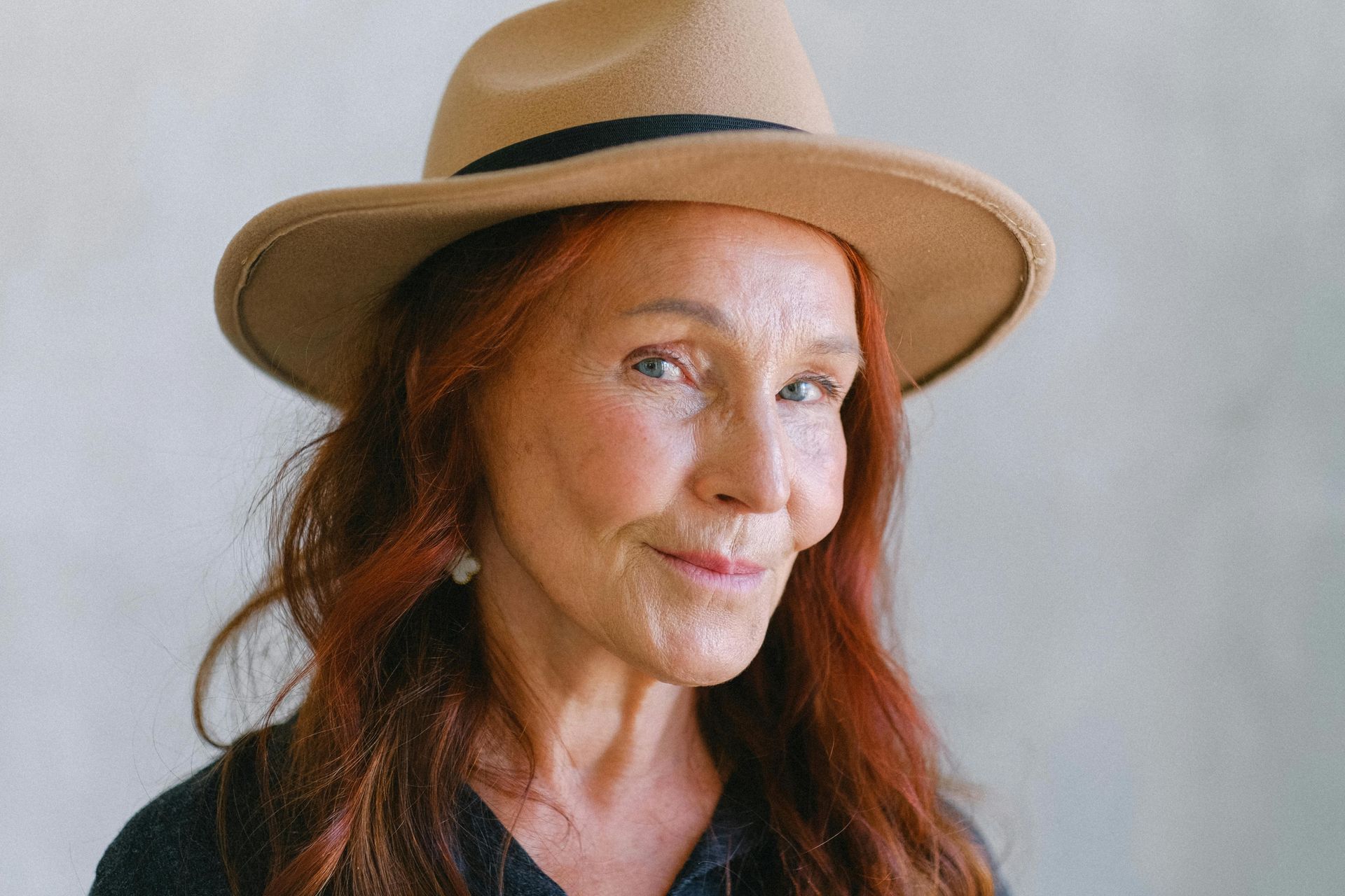Une femme aux cheveux roux porte un chapeau et sourit.