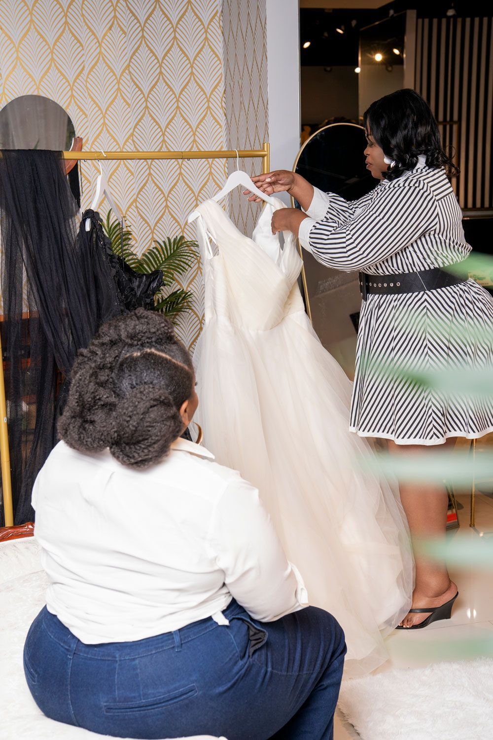 Three people adjusting a white dress on a rack in a boutique-like room