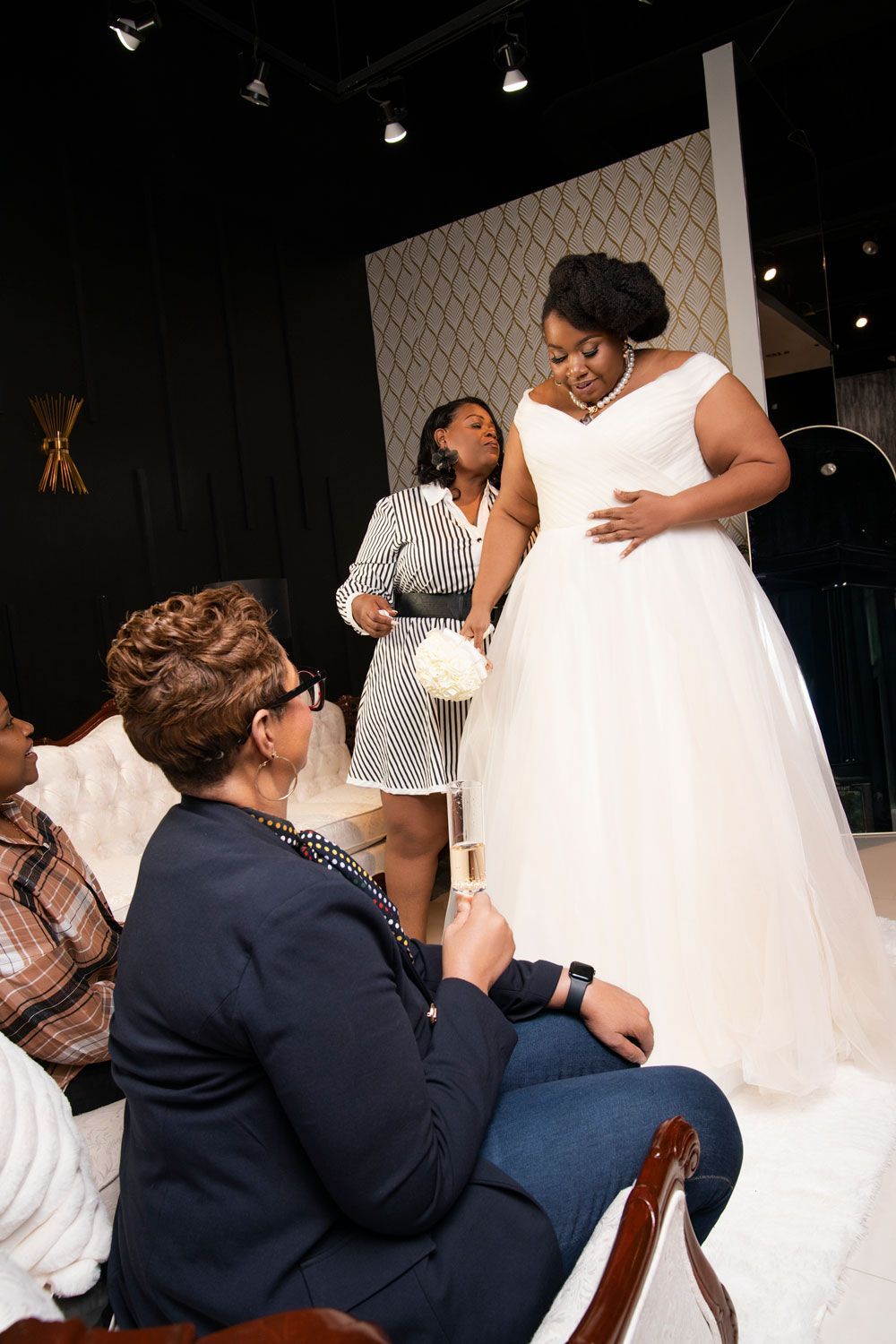 Woman in white dress on stage, adjusting her gown while seated guests look on in a dark venue.