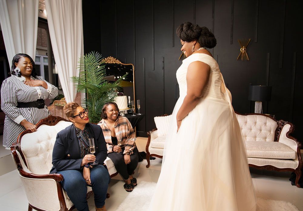 Bride in a white gown faces seated guests in a stylish living room during an intimate gathering