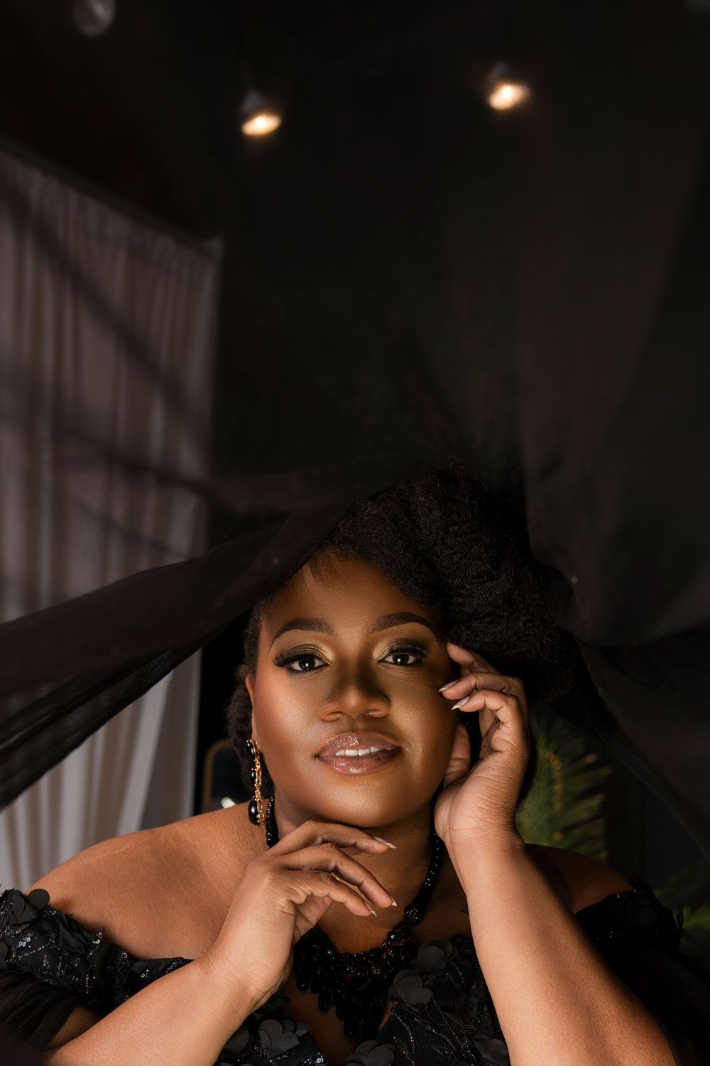 Portrait of a woman in a black dress, resting her face in her hands against a dark backdrop.