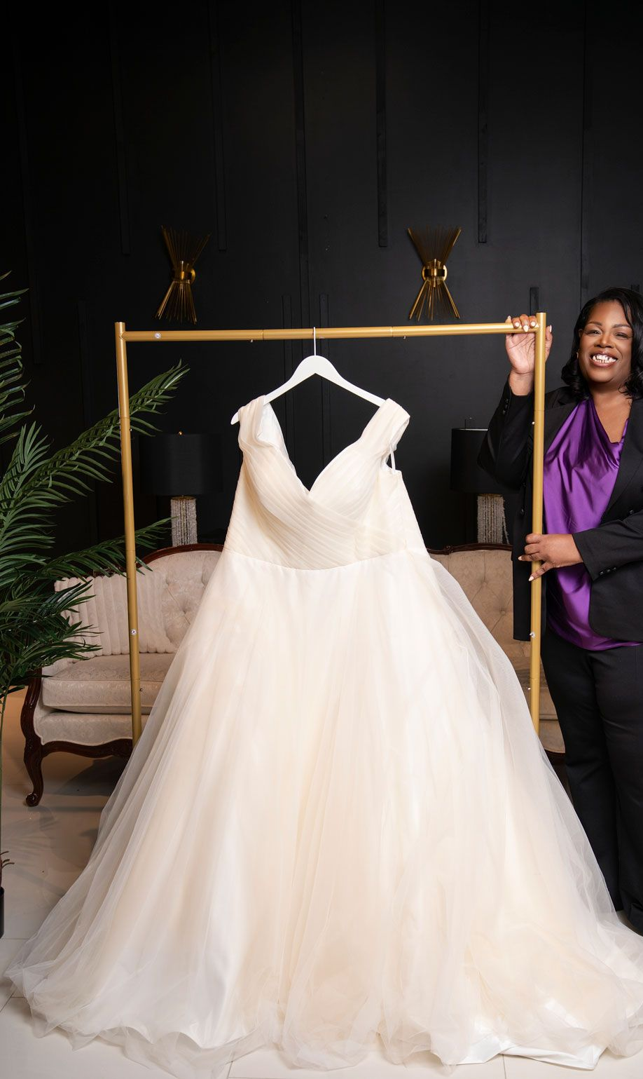 Woman standing beside a white wedding gown on a rack in a dim room